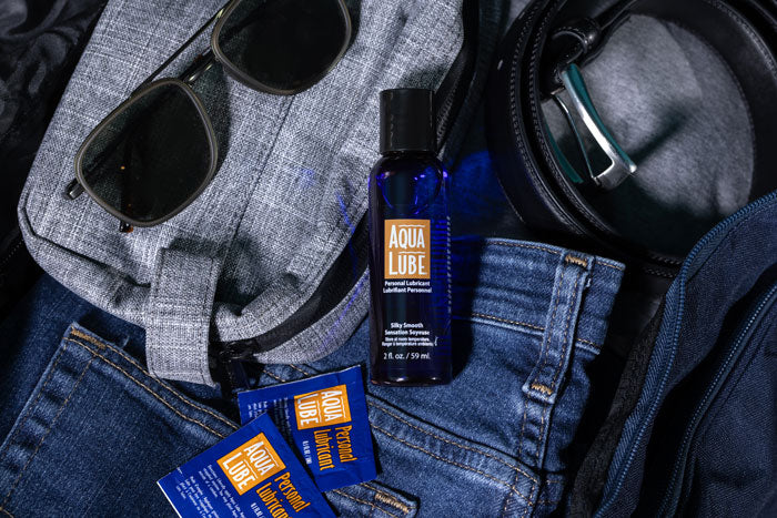 Aqua Lube product with sunglasses, jeans, and a belt on a dark surface